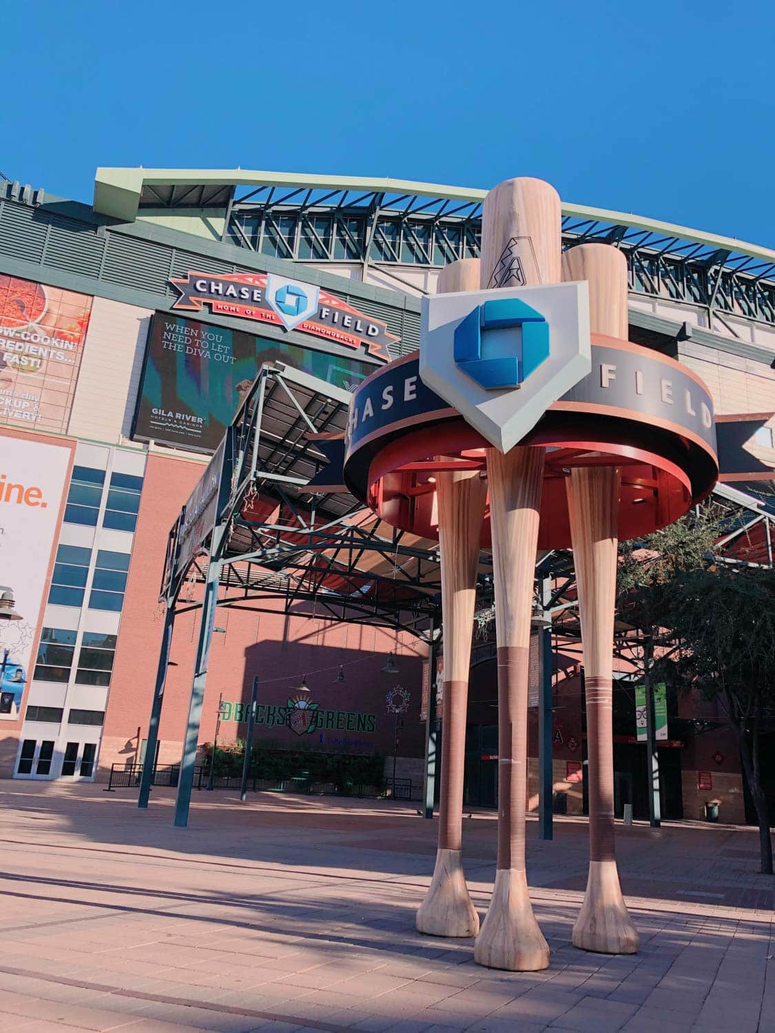 Exterior view of Chase Field, featuring a sculpture of large wooden baseball bats and the stadium’s signage under a clear blue sky in peoria az